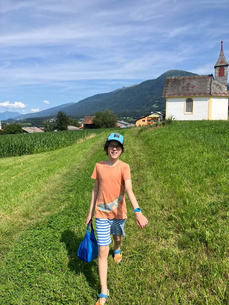 A child walking through a meadow toward a chapel near Innsbruck, with mountains in the background.