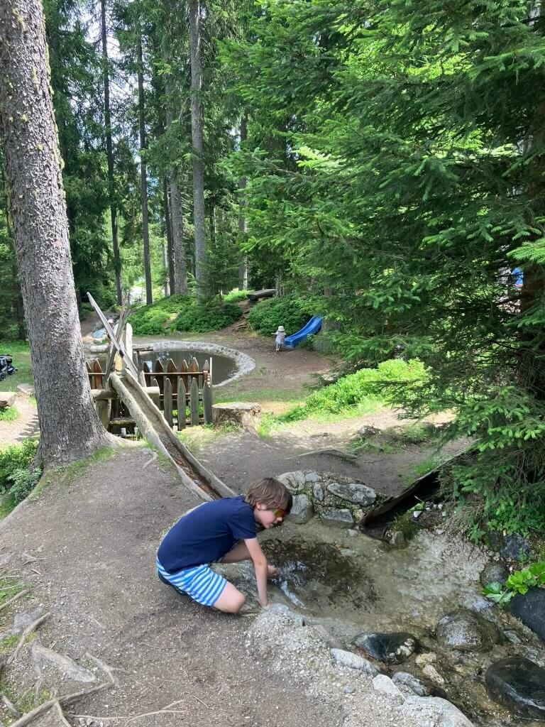 A child playing by a small forest creek near Innsbruck, surrounded by lush greenery and nature trails—a tranquil spot near Innsbruck for families seeking outdoor adventure.