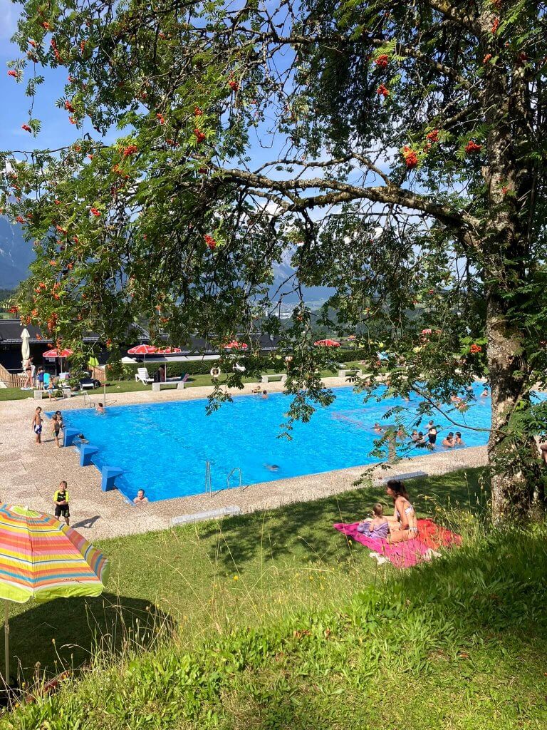 An outdoor swimming pool near Innsbruck, surrounded by green grass and trees, with mountain views—a family-friendly activity in Mutters, near Innsbruck.