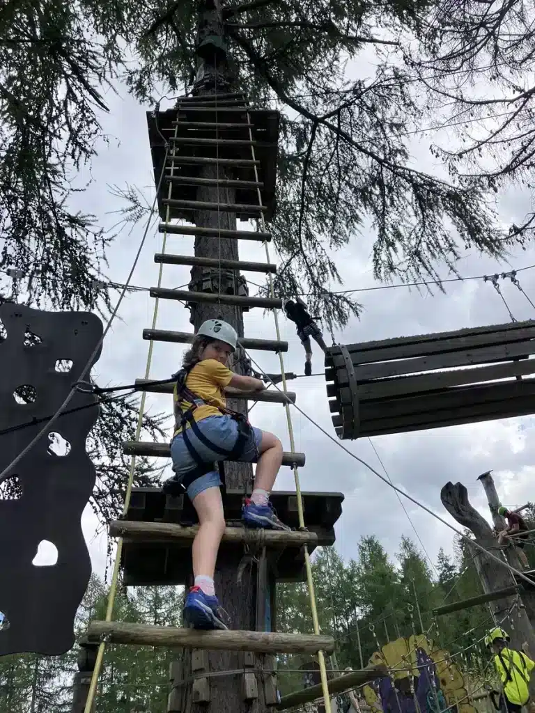 Wearing a harness and helmet, a child climbs a tall ropes course—an adventurous scene that reflects how raising resilient children through family travel builds courage.