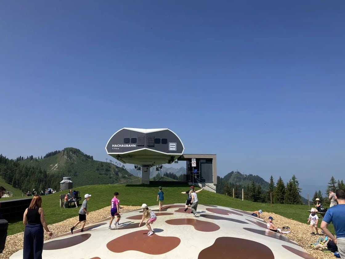 Kids bouncing on a giant trampoline painted with cow spots in front of the Hachau cable car station at Wagraini's Grafenberg—an unforgettable experience when visiting Wagrain with kids.