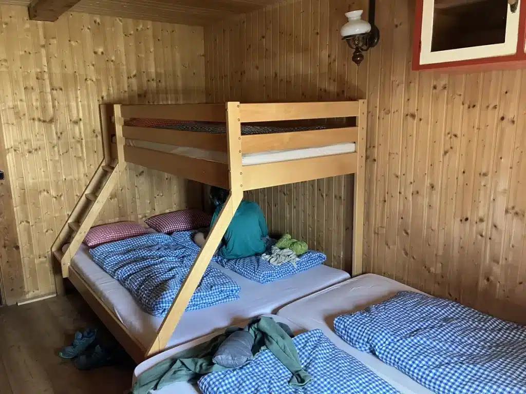 A cozy wooden bunk room with gingham bedding, offering simple overnight accommodation in a mountain hut.