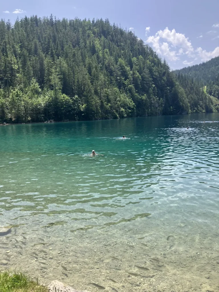 Swimmers relax in the crystal-clear waters of a forested mountain lake, a refreshing stop along the Wilder Kaiser hut to hut hike from Kufstein.