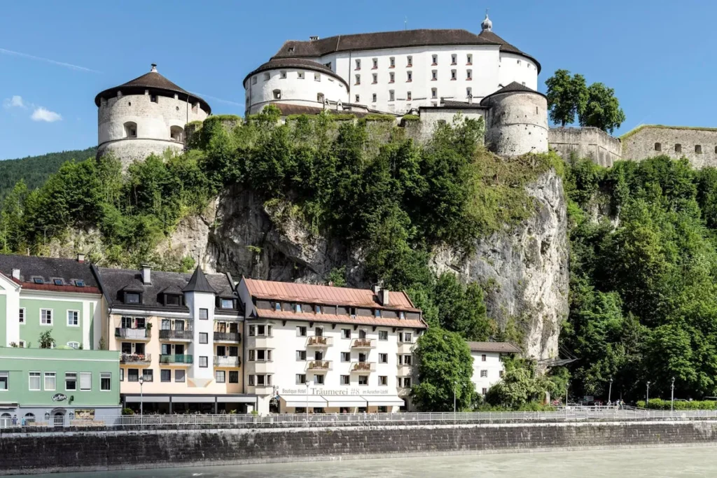 Kufstein Fortress towers above colorful riverside buildings and lush cliffs in the Austrian town of Kufstein, the scenic starting point of the Wilder Kaiser hut to hut hike.