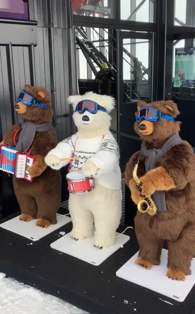 Three animatronic bears wearing ski goggles and scarves play musical instruments—an accordion, snare drum, and saxophone—outside a ski lift station in Les Arcs.