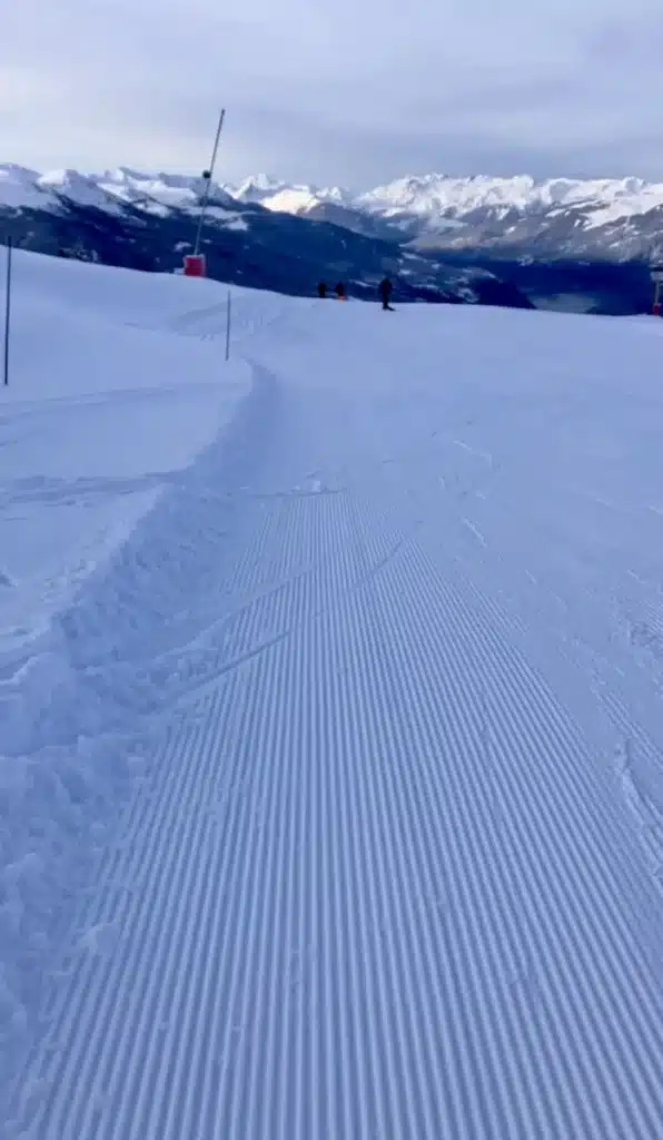 A wide, freshly groomed ski slope with corduroy snow patterns and panoramic mountain views in Les Arcs. A "First Tracks" experience is ideal for ski gift experiences.