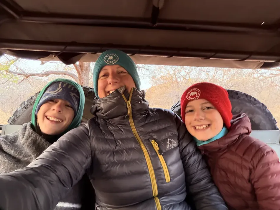 A woman and two children bundle up in puffer jackets and knit hats during a chilly safari drive. Their warm layers show why cold weather clothing can be useful even on an African safari.